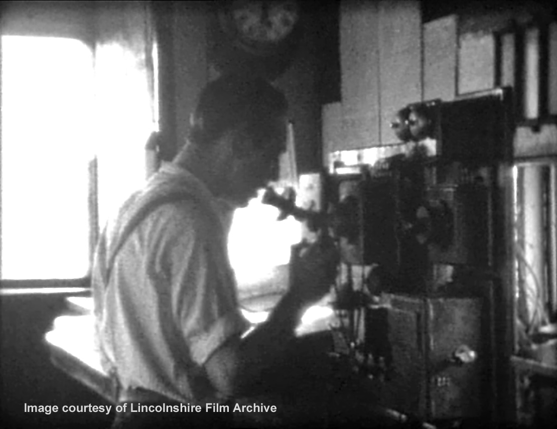 The telegraph lad on the telephone at the south end of the box. Behind him is the train register, where the time of every passing train and of every communication with other signal boxes was recorded. From a film shot by Walter Lee. © Lincolnshire Film Archive