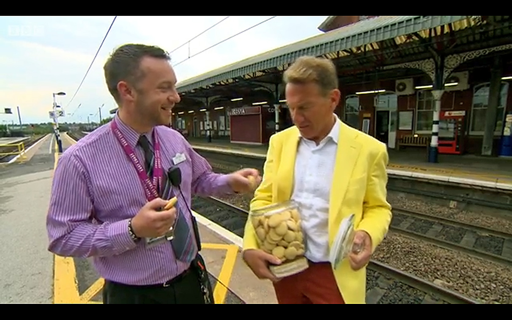 Michael Portillo shares his Grantham Gingerbread with a member of the East Coast staff at the station. From Great British Railway Journeys Series 6: 11 Derby to Grantham, © BBC