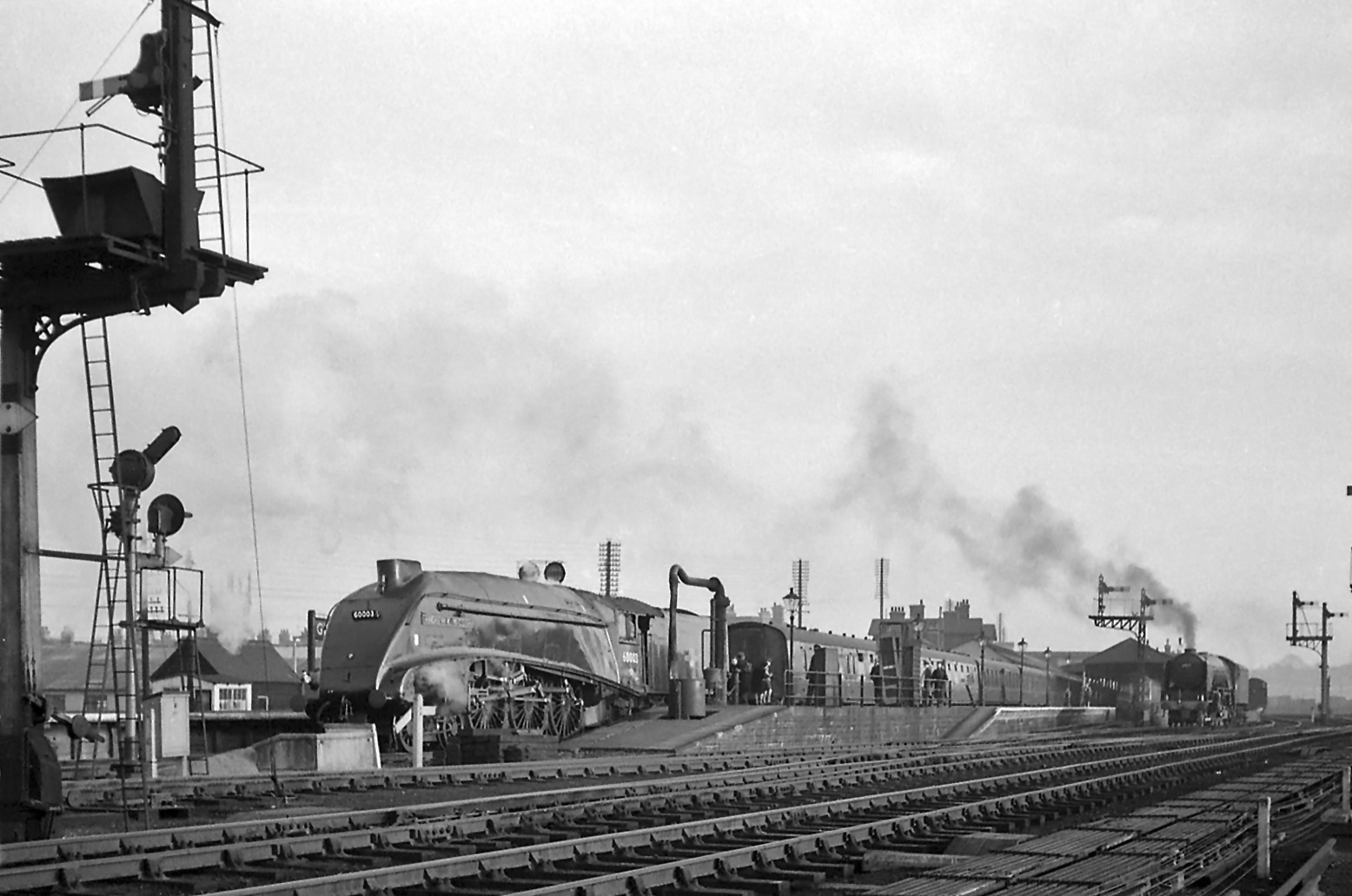 The Tees -Thames Express has arrived in platform 3. Class A4 No.60003 Andrew K McCosh has already been uncoupled from the train by one of Grantham's passenger shunters. It is drawing forward, will pass the signal box and move across to the Nottingham line before reversing back to the shed, when it will pass close to where Noel is standing. No. 60517 is still waiting in the right background, its fireman making final preparations by building up the fire. Photograph by Noel Ingram, used with permission from Steam World.