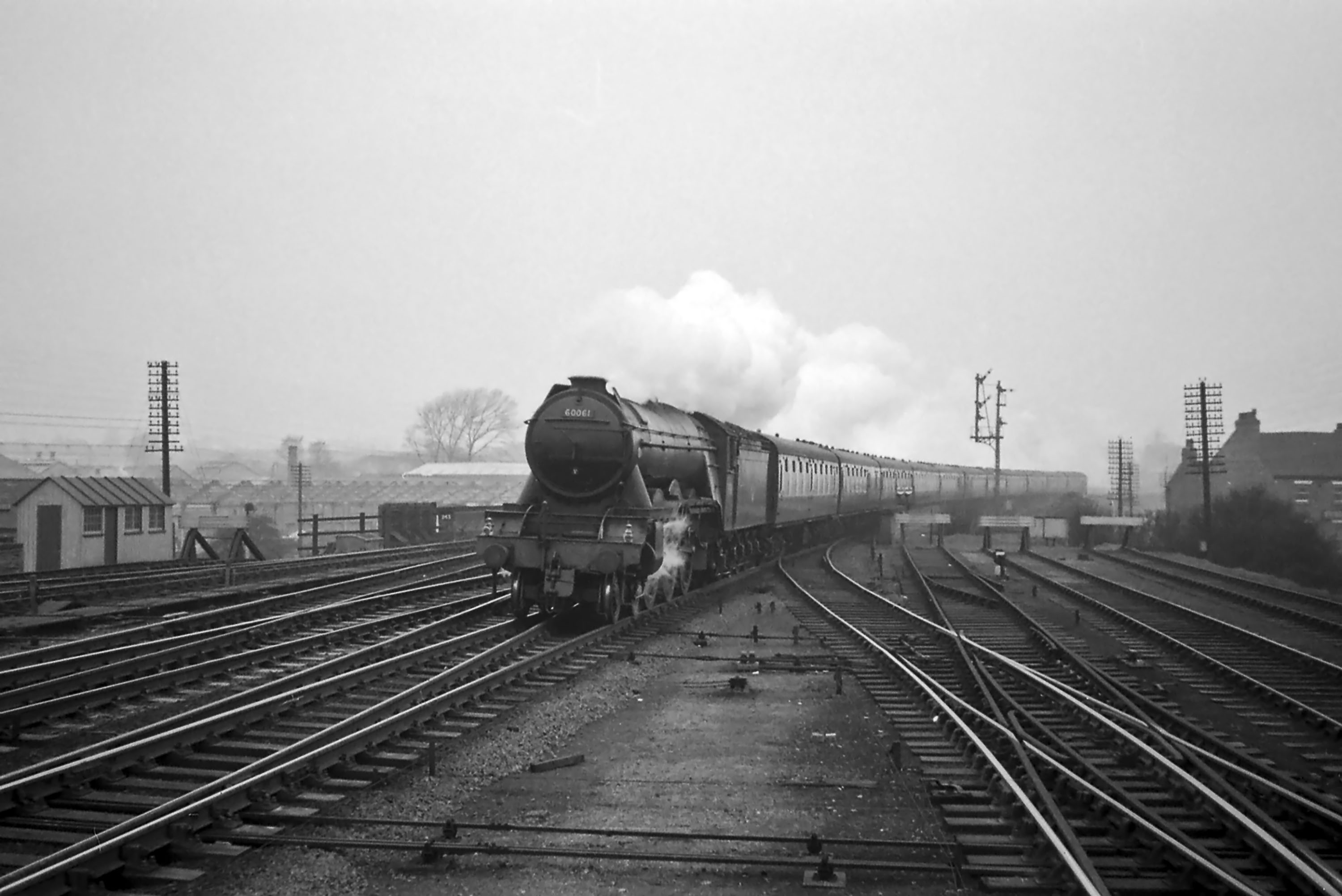 This photograph was taken from the north end of the Up (southbound) platform, opposite Grantham North box (which was just off shot to the left). It’s not possible to reach this spot today because the Up platform was cut short in the late 1960s. The first coach of this southbound train on the Up Main line, hauled by No.60061 Pretty Polly, is passing over the connection to the Up Bay platform. The Nottingham lines are converging into the Main lines from the left. We can see that the train is not stopping at the station because both the Grantham North box Up Main home signal and, beneath it, the Grantham Yard box Up Main distant signal are showing ‘clear’. To the right of the Main Line signals is the signal for the Up Bay platform. It’s worth pointing out here the two lines of telegraph poles, one on each side of the railway, which used to be so much part of the everyday railway scene. These pole routes carried the block telegraph, the ‘speaking' (single needle) telegraph, telephone and other circuits on which the railway depended for the communication vital to effective operation. It was the responsibility of the Signal and Telegraph (S&T) Engineers and Technicians to maintain this widespread network and also to keep the signals maintained and in working order. It was a job that often involved working at height exposed to the worst of the weather. Photograph by Noel Ingram, used with permission from Steam World.