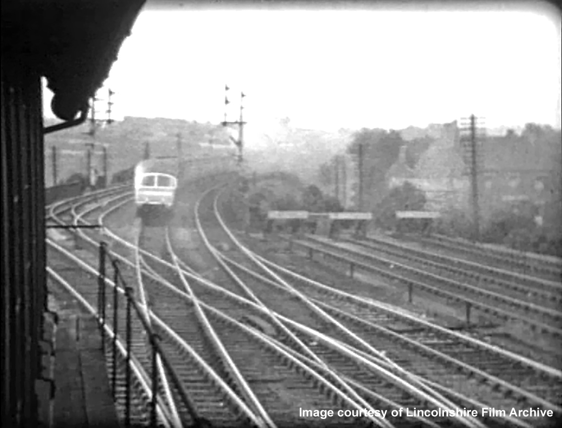 Viewed along the eastern side of the box in 1937, the junction for Nottingham is in the foreground. Leading in from lower right are connections from the Up Bay platform, loading dock and sidings. On the extreme left is a connection from the Down Nottingham line to the Up Nottingham line, which enabled locos off the shed to access the Up Main line through the station to Grantham Yard box, for locomotive changes on southbound trains. The Coronation service recedes at speed on the Main line towards Barrowby Road, its unique Observation Car bringing up the rear. Taken from a cine film shot by photographer and film maker Walter Lee of Grantham. © Lincolnshire Film Archive