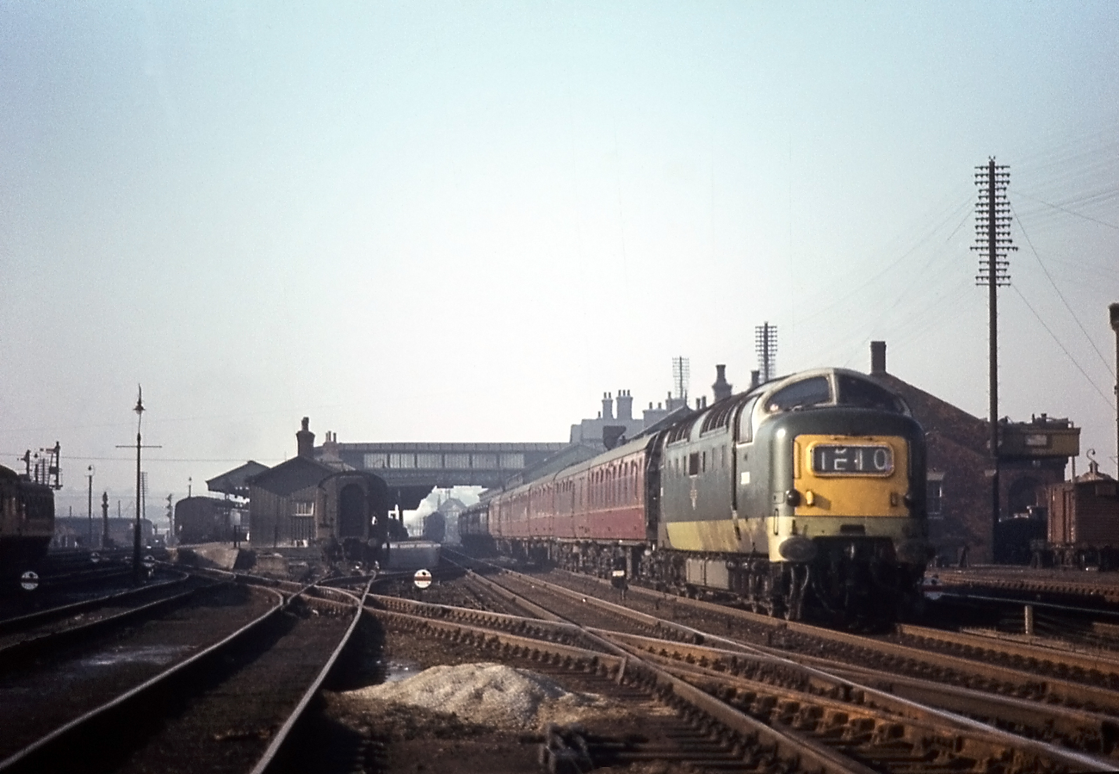  This is the approach to the station from the south in the early 1960s. It was taken from between the Main lines, on the right, and the Down Slow line on the left. Beyond the Down Slow line is Carriage Siding No.1. The roof of Grantham Yard box can be glimpsed above the front of the first coach of the approaching train. All the connections with the line which crosses diagonally from the bottom right corner to the Western platform on the left were under the control of Grantham Yard box. The disc signals facing the camera control shunting movements towards the station platforms. On the right the lofty pole route carries telegraph and telephone communication along the eastern side of the railway. Photograph by Noel Ingram, used with permission from Steam World.