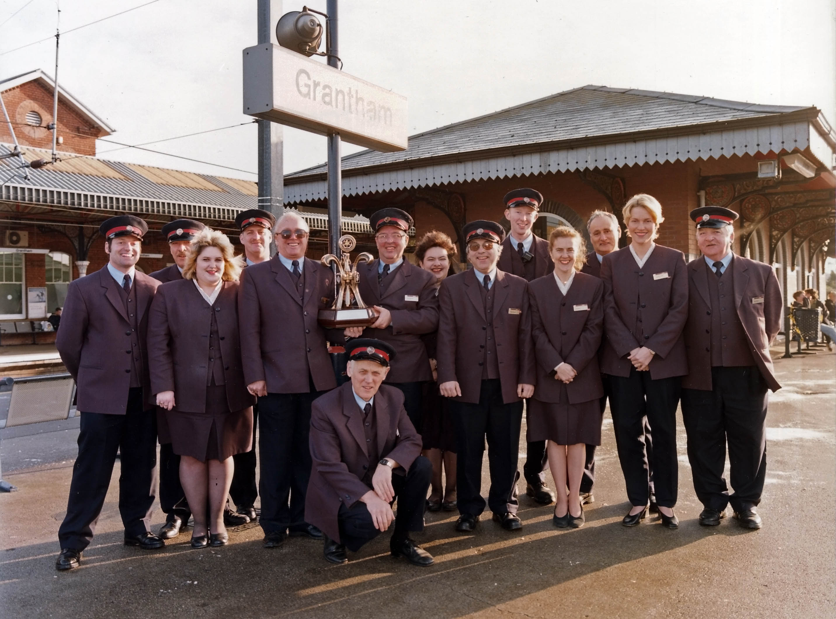 Station Staff in October 1998 with the Station of the Year trophy. Back row: Phil Beck, Paul Simons, Sharon Feeley, David Fielding, Barry Booth (train crew roster clerk). Middle row: ...unknown, Emma Norris, Tom ..., John Starbuck, Roger Prior, Val Markham, Caroline ..., Mick Gibson. In front: Derrick Pegg. Photograph by Fastline Photographic, kindly lent by John Starbuck.