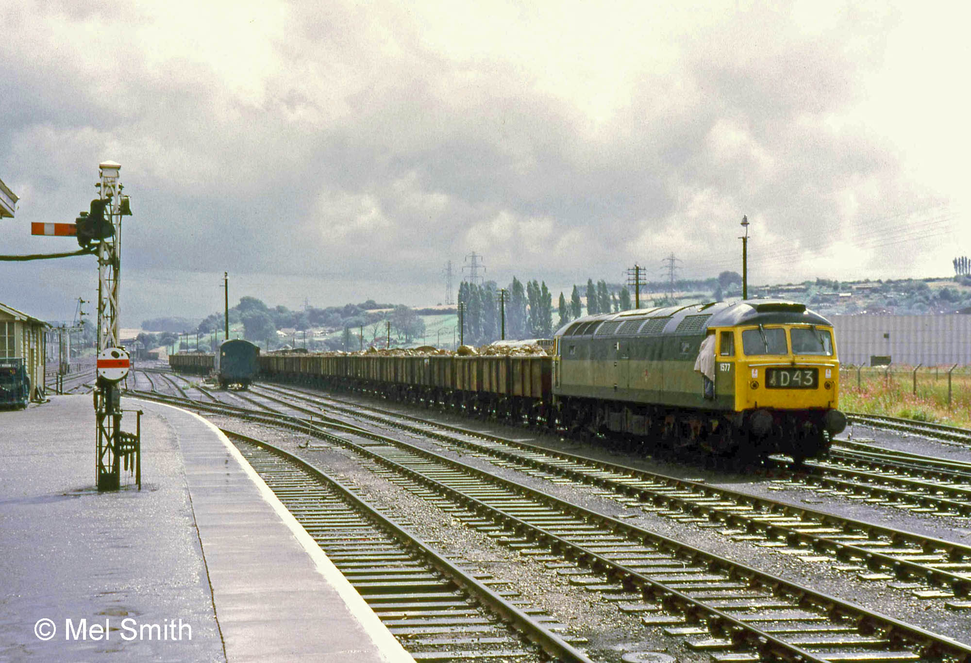 This is a view of the south end of the Western platfrom in early summer 1971 (before 27th June, when the Yard Box closed). The signal on the Western platform controls access to the south, either along the Down Slow line towards the South Box (the upper arm) or into No.1 Carriage Siding (the disc signal). In the distance to its left is the signal controlling the Down Slow line as it approaches the Western platform from the south. In the far distance, just to the right of the disc, is Grantham South box. The carriage sidings are virtually unoccupied. Class 47 No.1577 has charge of an ironstone train on the Up and Down Goods line. Photograph by Mel Smith.