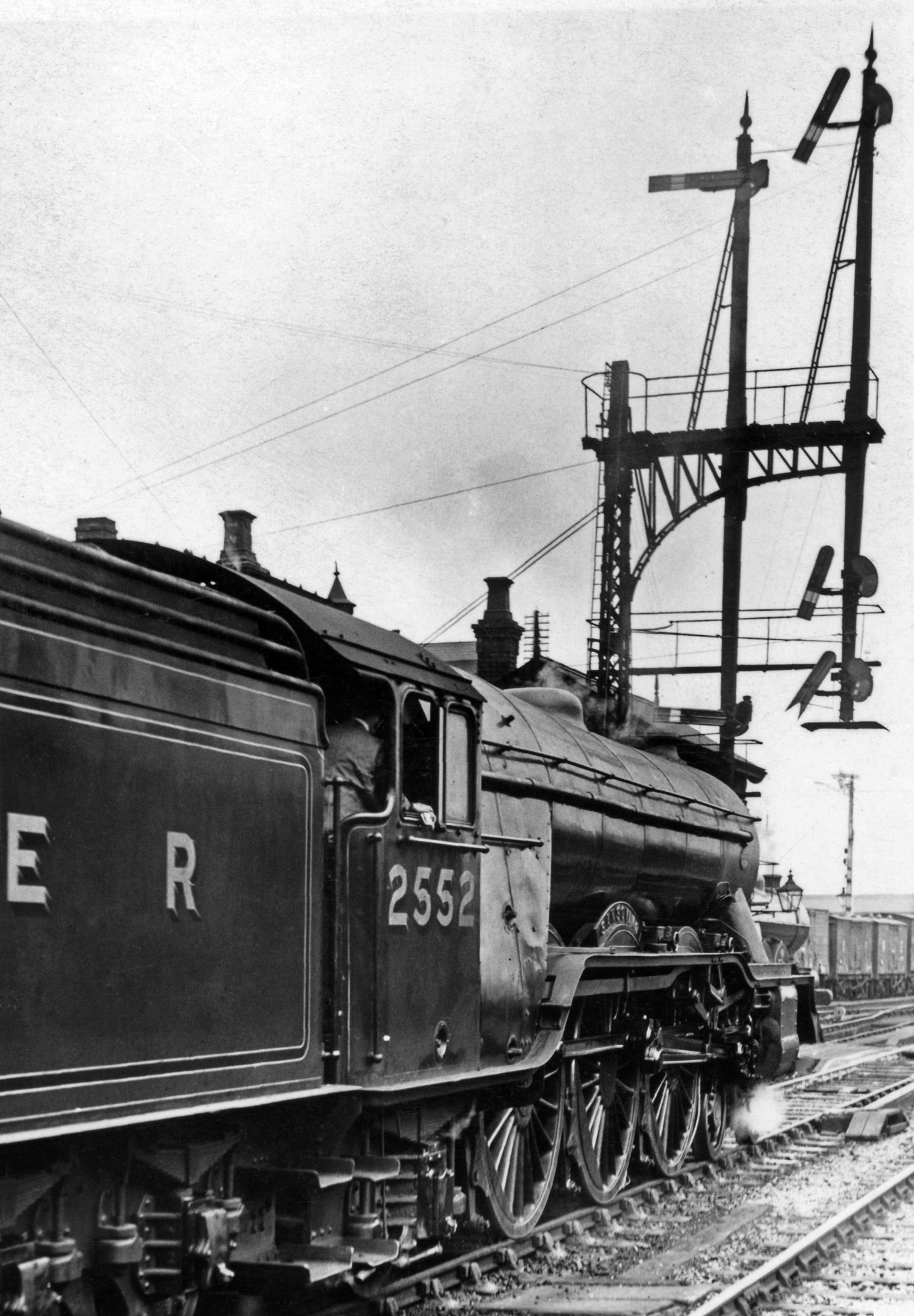 The lofty Grantham Yard Box Up starting signal overshadows handsome A1 locomotive No.2552 Sansovino, whose crew are making ready to depart for the south. The signal shows 'clear' for the Main line into and through the section controlled by Grantham South box - the lowest arm, with the vee end, is the South Box distant signal. The two high-level arms are 'co-acting' with the corresponding main arms beneath them. Signals had to be visible from a distance to give drivers time to respond, and the high-level arms and their lamps could be seen over the staion footbridge from the footplate of an approaching train . They are also larger in size, to aid sighting from a distance. The signals on the left relate to the Up Goods line, which diverges to the left just beyond the platform. They were positioned at a lower level because it was the less important route. There are several sturdy stays to support the overhanging weight of the bracket and its equipment. This scene dates from the late 1920s or the 1930s. In the late 1930s or the 1940s the GNR 'somersault' signal arms were replaced by modern upper quadrant arms. Photograph by courtesy of Graham Cloxton.