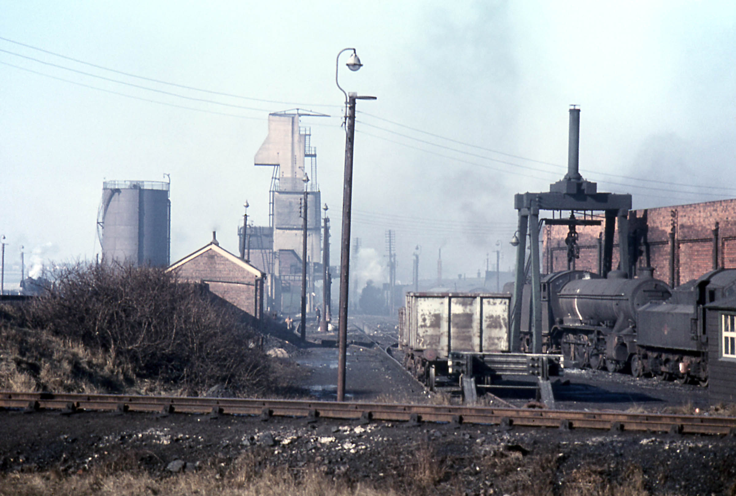 A view up the Loco yard from the south, with the top shed on the right. Across the foreground is a spur which forms an apex of the 'angle', the shed's turning triangle. It endsJust off shot to the right, facing the side wall of the shed. At the extreme right is a corner of the wooden shed which was used for instruction classes. Photograph taken by Noel Ingram, used with permission from Steam World.